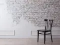 Silla negra frente a pared de ladrillo rústica, con un acabado de pintar pared de piedra en blanco que deja ver la textura original.