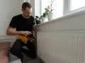 A man in a tool belt inspects a white radiator, checking for any signs of a cracked radiator before winter sets in.