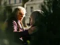 A man with white, curly hair and a mustache gently places his hand on another person's shoulder, offering a comforting response. This scene illustrates react vs respond examples.