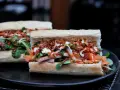 Zwei appetitliche Banh Mi Sandwiches mit Fleisch, Gemüse, knusprigen Zwiebeln und Saucen auf einem Teller.