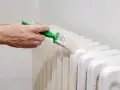 Main d'une personne peignant un radiateur en fonte avec une brosse.