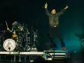 Linkin Park-Bandmitglieder auf der Bühne, ein Sänger springt, ein Schlagzeuger spielt.