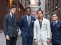 Quattro uomini in abiti eleganti, con un impeccabile bavero giacca, posano in un vicolo urbano.