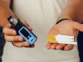 Man holds a vape in one hand and cigarettes in the other, posing the question: que es mejor el vaper o el tabaco.