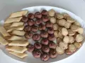 En vit oval bricka fylld med tre sorters hembakade småkakor: rombiska, chokladpraliner och runda med strössel. Perfekt för fika!