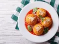 Quattro arancini di riso dorati, cosparsi di parmigiano e serviti su un letto di salsa di pomodoro, guarniti con basilico fresco.