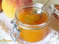 Cuchara con mermelada de melocotón casera, junto a melocotones frescos y un tarro de cristal.