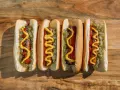 Cuatro hot dogs con mostaza, kétchup y cebolla picada sobre una tabla de madera.