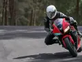 Motocyklista w białym kasku i czarnym kombinezonie pochyla się na czerwonym motocyklu podczas jazdy po drodze.