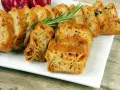 Tranches d'un cake salé au chorizo et poivron, garni de romarin, sur une assiette blanche.