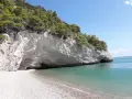 Una spiaggia di ciottoli bianchi si apre su un mare cristallino, incastonata tra imponenti scogliere calcaree ricoperte di pini marittimi. Sembra proprio la baia delle sirene, un luogo incantato.