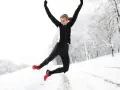 Glad kvinna hoppar i snön, njuter av att springa i kyla. Vinterlandskap med träd.