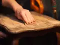Main d'une personne ponçant un meuble en bois pour enlever la cire naturellement.