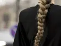 Gruby, blond warkocz opada na czarne ramię. To jedna z tych fryzur z warkoczem, które przyciągają wzrok.