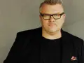 Rafał Michalak w czarnym garniturze i okularach, z charakterystyczną bródką. W kieszeni marynarki ozdobna poszetka.