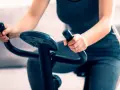 Kobieta ćwiczy jazdę na rowerze stacjonarnym w domu, skupiona na treningu.