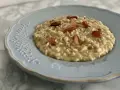 Un cremoso risotto con ceci e pancetta croccante, servito su un piatto azzurro decorato.
