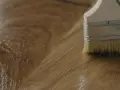 Brocha aplicando un acabado brillante sobre madera, mostrando diferentes tipos de barniz para madera.