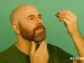 Hombre calvo con barba hipster, aplicando aceite con un gotero.