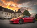 Czerwone Ferrari zaparkowane przed zabytkowym budynkiem podczas zachodu słońca.