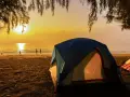 Kameralne pole namiotowe nad morzem. Słońce wschodzi nad spokojnym oceanem, rzucając złoty blask na plażę i namioty.