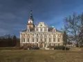 Imponujący zamek w Roztocze, z charakterystyczną wieżą i bogato zdobioną fasadą, otoczony parkiem.