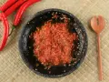 Świeżo przygotowany sos sambal w kamiennym moździerzu, obok czerwone papryczki chili i drewniana łyżka.