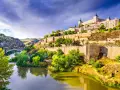 El **río Tajo** serpentea al pie de Toledo, una ciudad amurallada coronada por un imponente alcázar. Un puente de piedra cruza el agua, conectando las verdes orillas.