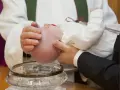 Chrzest chłopca: biała szatka, szklana chrzcielnica i woda święcona.