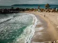 Piękne, turkusowe morze w Bułgarii obmywa piaszczystą plażę. W oddali widać wzgórza i samochody.