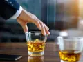 Hand greift nach einem Glas goldbraunen Whiskey mit Eiswürfeln. Ein Genuss, auch für Menschen, die glutenfreien Whiskey bevorzugen.