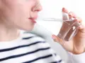 Kobieta pije wodę z szklanki, by zwalczyć suchość w ustach.