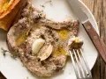 Succulenta braciola di maiale cotta con aglio e erbe aromatiche, servita con pane croccante.