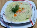 Aromatyczna zupa koperkowa z ryżem, kawałkami kurczaka i marchewką, udekorowana gałązką koperku.