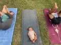 Un bébé sur un tapis de yoga, entouré de ses parents pratiquant le yoga. Une séance de yoga pour enfants en plein air.