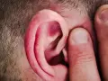 Un doigt pince l'oreille d'un homme, comme pour mieux capter un son aigu.