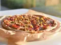 Apetyczna pizza Giuseppe 4 sery, z kukurydzą i mięsem, na papierze do pieczenia, w słonecznym świetle.