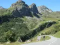 Ciclista su strada tortuosa verso il Cormet de Roselend, con montagne imponenti e verdi pendii.