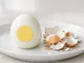 Un œuf dur coupé en deux, montrant son jaune parfait, à côté de sa coquille ébréchée. La cuisson de l'œuf dur est réussie.