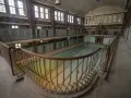 Verlassenes Stadtbad, das auf eine "Reloaded"-Zukunft wartet. Verrostete Geländer umgeben das leere Becken, während die alten Umkleidekabinen still verharren.
