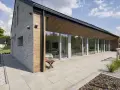 Nowoczesny dom z dużymi przeszkleniami i tarasem. Widać układanie płyt tarasowych na podsypce, tworząc estetyczną przestrzeń.