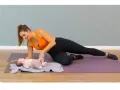 Une femme fait du sport après accouchement, en position de planche latérale, avec son bébé à ses côtés.