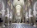 Wnętrze katedry Notre Dame, z monumentalnymi kolumnami, sklepieniem i witrażami. Na środku nawy stoi samotna postać.