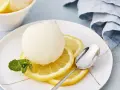 Erfrischendes Zitronensorbetto-Rezept: Eine Kugel Sorbet auf Zitronenscheiben mit Minze und Löffel.