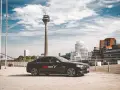 Schwarzer Wagen mit FREE NOW Logo steht vor dem Rheinturm in Düsseldorf. Ein FREE NOW Fahrer wartet auf seine Fahrgäste.