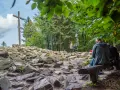 Kamieniste szlaki Gór Świętokrzyskich prowadzą do krzyża na szczycie. Ludzie odpoczywają na ławkach, podziwiając widoki.