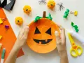 Barn gör halloween pyssel med en pumpa av papper. Små pumpor, spindlar och glitterpennor ligger redo.