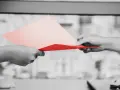 Dwie dłonie przekazują sobie dokumenty. Jedna z nich trzyma różową kartkę, druga czerwoną. Symbolizuje to uprawomocnienie postanowienia sądu.
