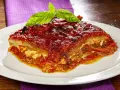 Una fetta di parmigiana di melanzane napoletana, ricca e saporita, guarnita con basilico fresco.