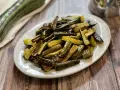 Zucchine al forno dorate e saporite, tagliate a bastoncini e servite su un piatto bianco.